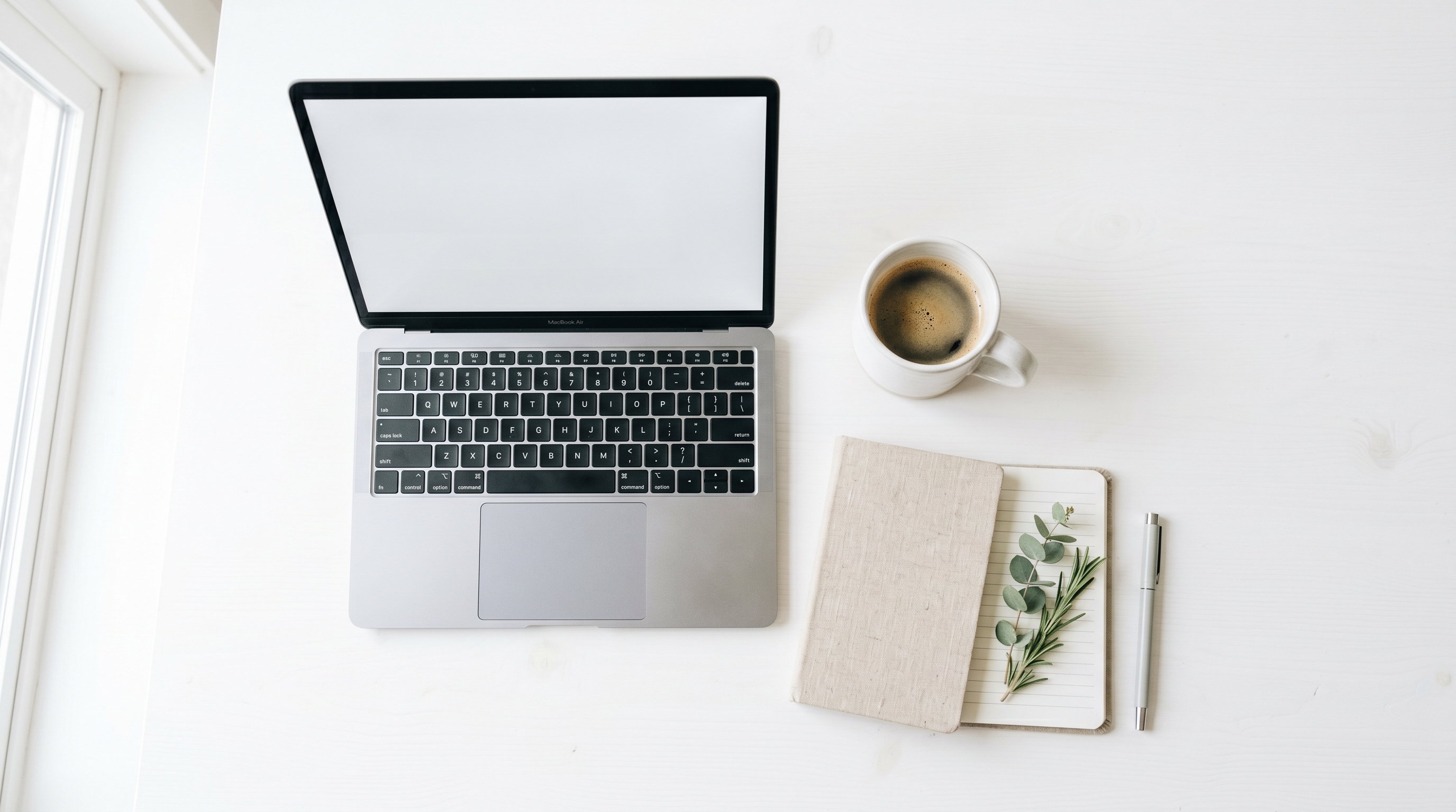Scrivania minimalista e luminosa con portatile, caffè e taccuino